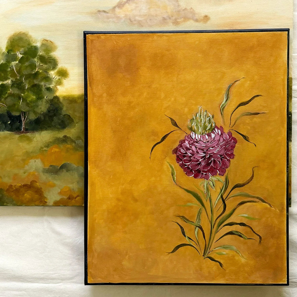 A framed original painting featuring a textured mustard-yellow background with a detailed illustration of a deep red ranunculus and green leaves