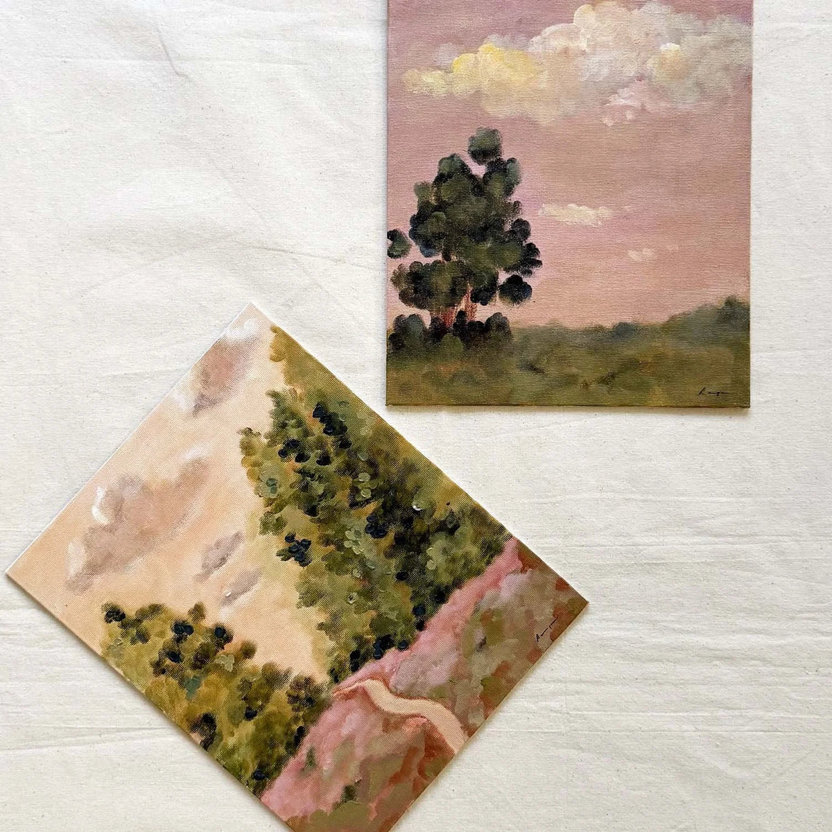 Two small original landscape paintings, one showing a tree under a pink sky and the other showing trees and a pale path