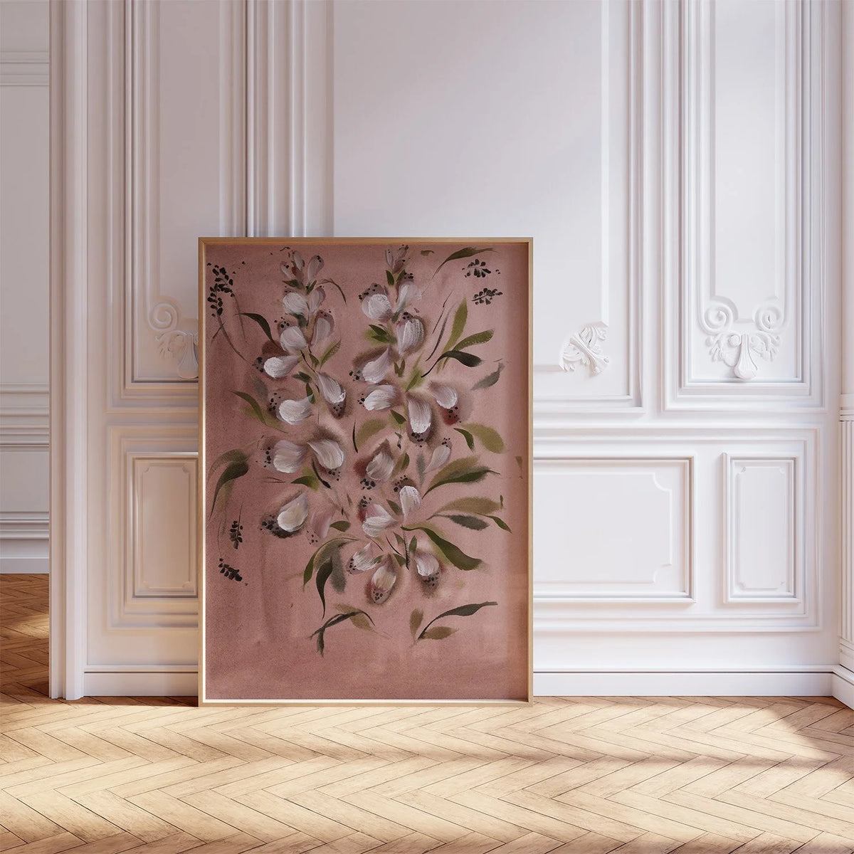 A vertical framed botanical art print featuring white flowers with green leaves on a dusty rose background, leaning against a white paneled wall on a light wood herringbone floor.
